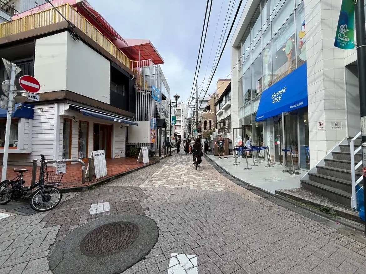 - おしゃれなカフェやショップが並ぶ賑やかな通り、歩道には人々が行き交い、自転車が置かれた風景