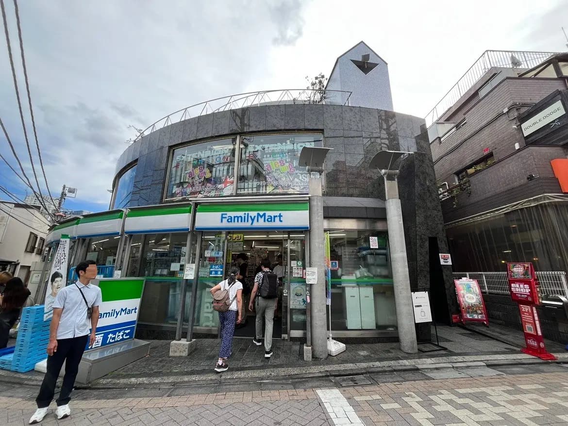 ファミリーマートの店舗外観、モダンなデザインの建物、店舗前に並ぶ客と看板、周囲に商業施設が立ち並ぶ街並み