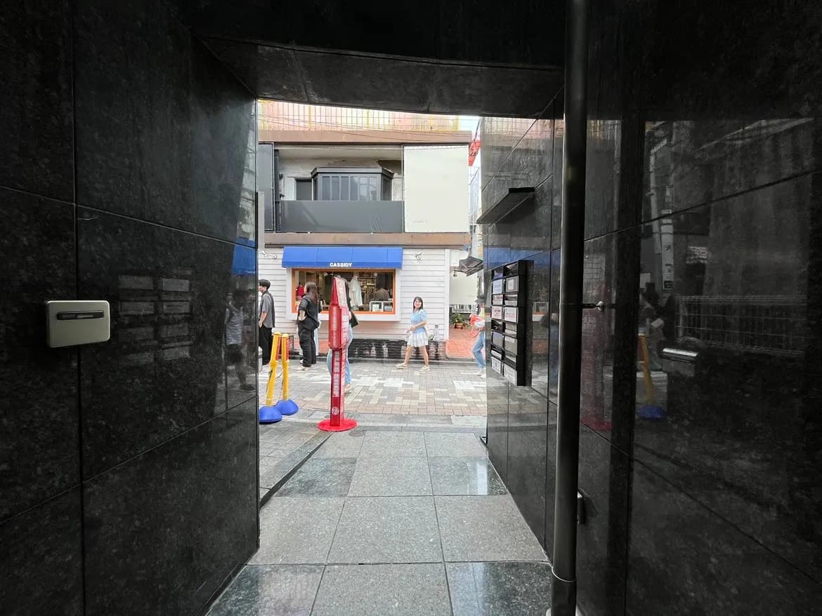 - 石造の入口から見える街並み、カフェの看板や行列、歩行者が行き交う賑やかな通りの風景