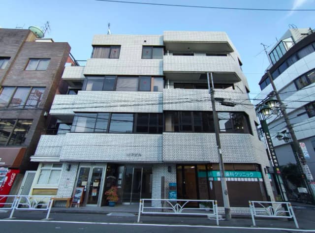 - 白いタイルの外観の商業ビル、窓が大きく明るい印象、道路沿いに位置する歯科クリニックの看板が見える景観