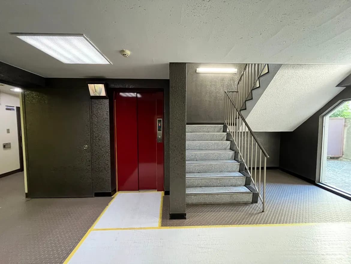 - モダンなエレベーターと階段がある建物のエントランス、シンプルなインテリアデザインと明るい照明が特徴