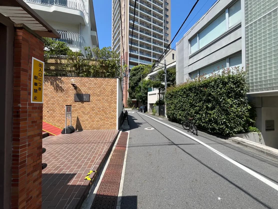 - 都市の住宅街の一角、レンガ造りの壁と駐車禁止の標識、周囲には高層ビルと緑豊かな植栽が配置された風景