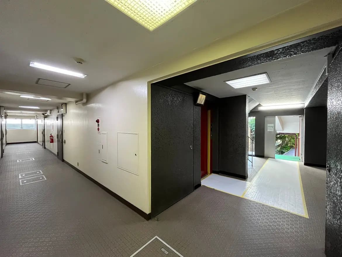 - 明るい照明が点灯した住宅の廊下、壁は白色で、エレベーターと非常口の標識がある静かな空間の内装