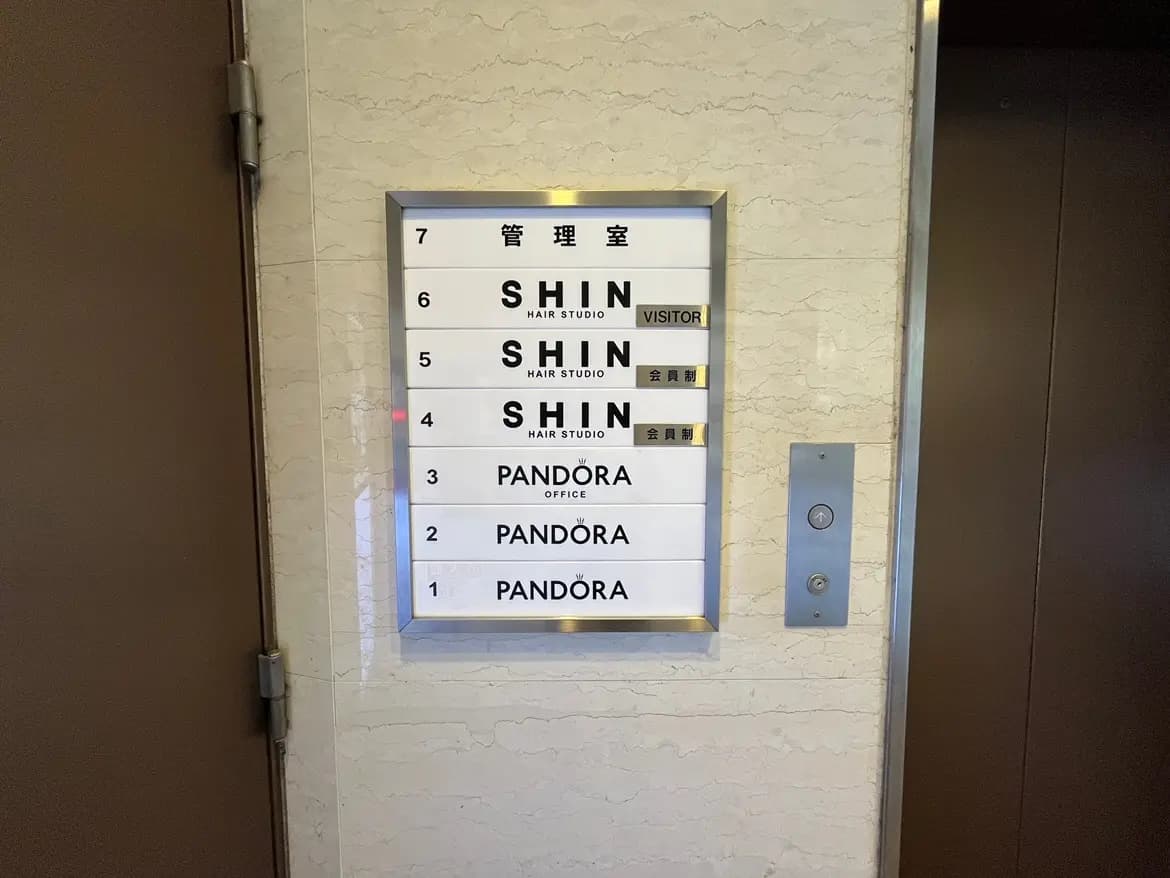 - エレベーター内のフロア案内板、ヘアスタジオ「SHIN」やオフィス「PANDORA」の表示がある清潔感のあるデザイン