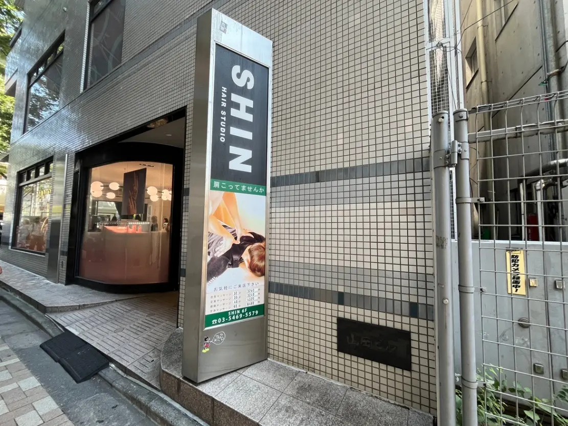 - 東京の美容室「SHIN」の外観、スタイリッシュな看板とモダンなデザインの入り口、周囲の街並みが見える景観