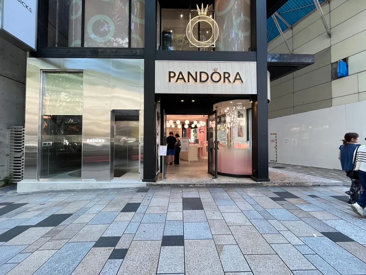 - 銀色の外観を持つ「PANDORA」店舗の入り口、周囲に人々が行き交う賑やかな通りの風景