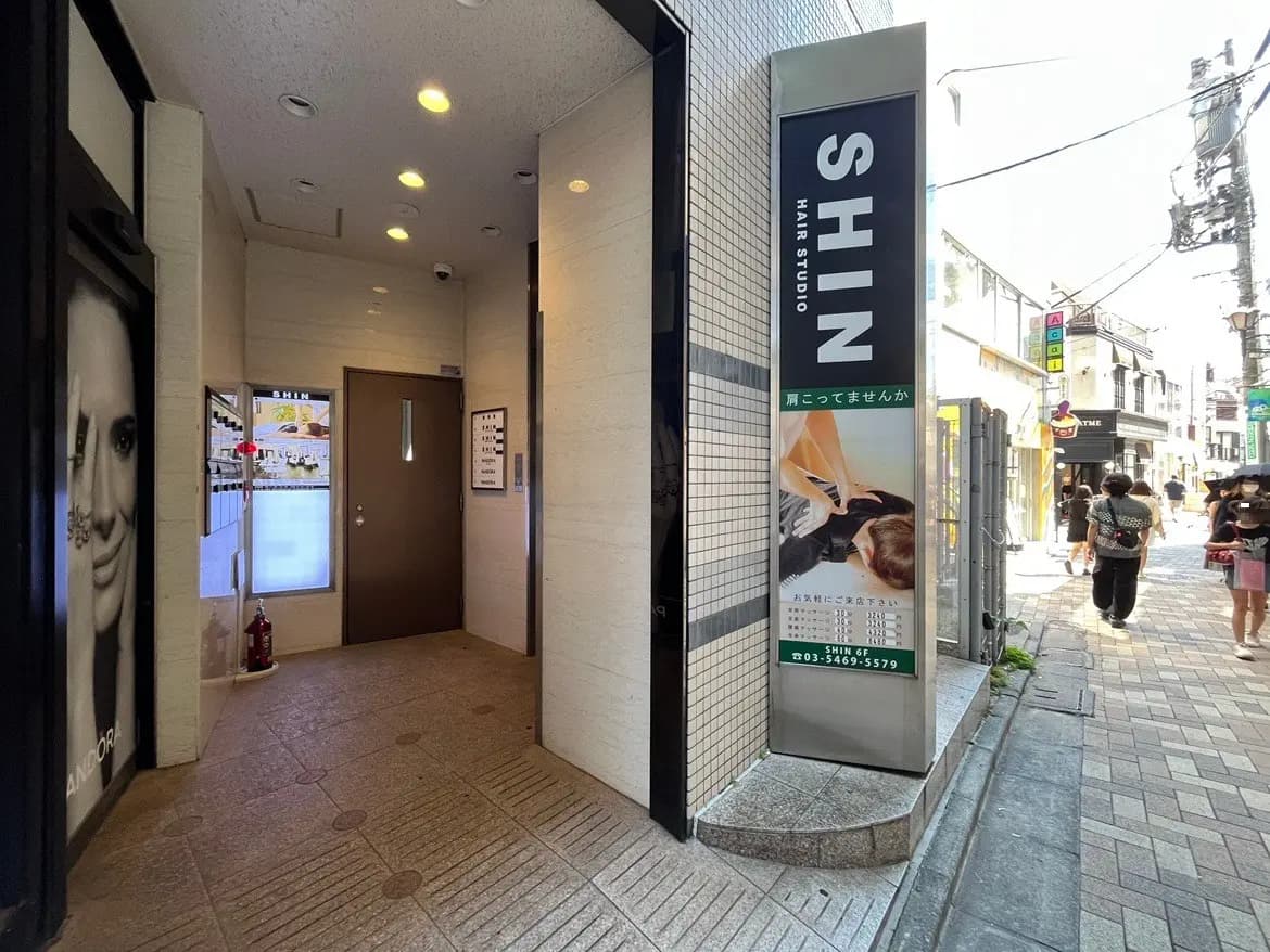 - 髪の毛のスタイリングを施している美容室「SHIN」のエントランス、明るい通りに面した入口と店名看板が見える街の風景