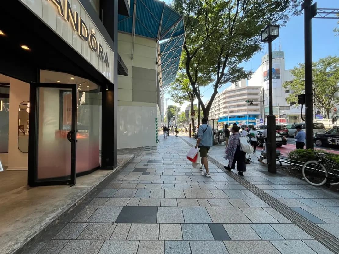 - ショッピング街の歩道、カフェと店舗が並ぶ、青空の下を歩く人々と自転車の風景