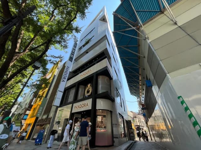 - おしゃれな商業ビル「PANDORA」の外観、繁華街の通りと木々が映える日中の風景、高い建物と人々の賑わい