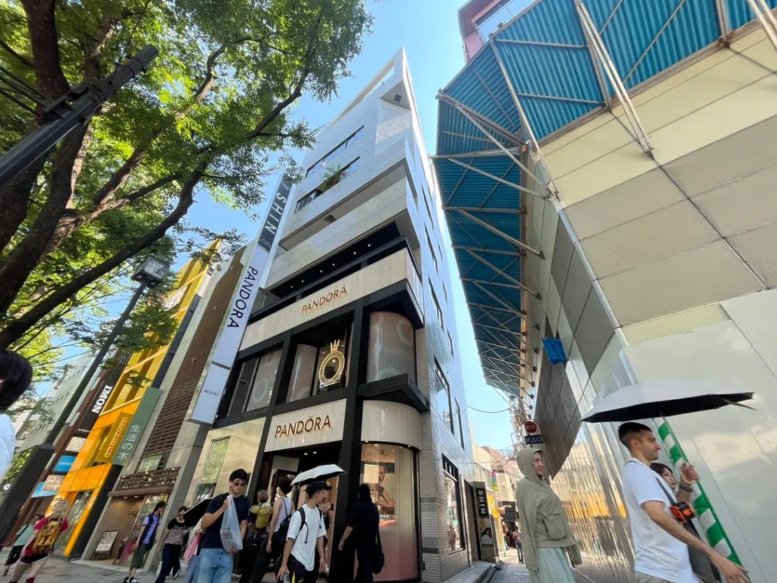 - ショッピング街にあるPandoraの店舗、現代的なデザインの建物と青空、行き交う人々が映る活気ある風景