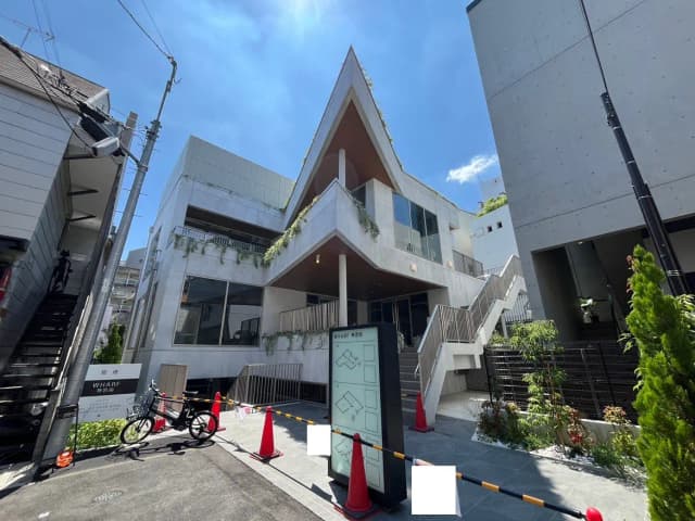 - モダンなデザインの建物外観、階段、緑の植栽が施されたエントランス、晴れた空の下に広がる都市風景