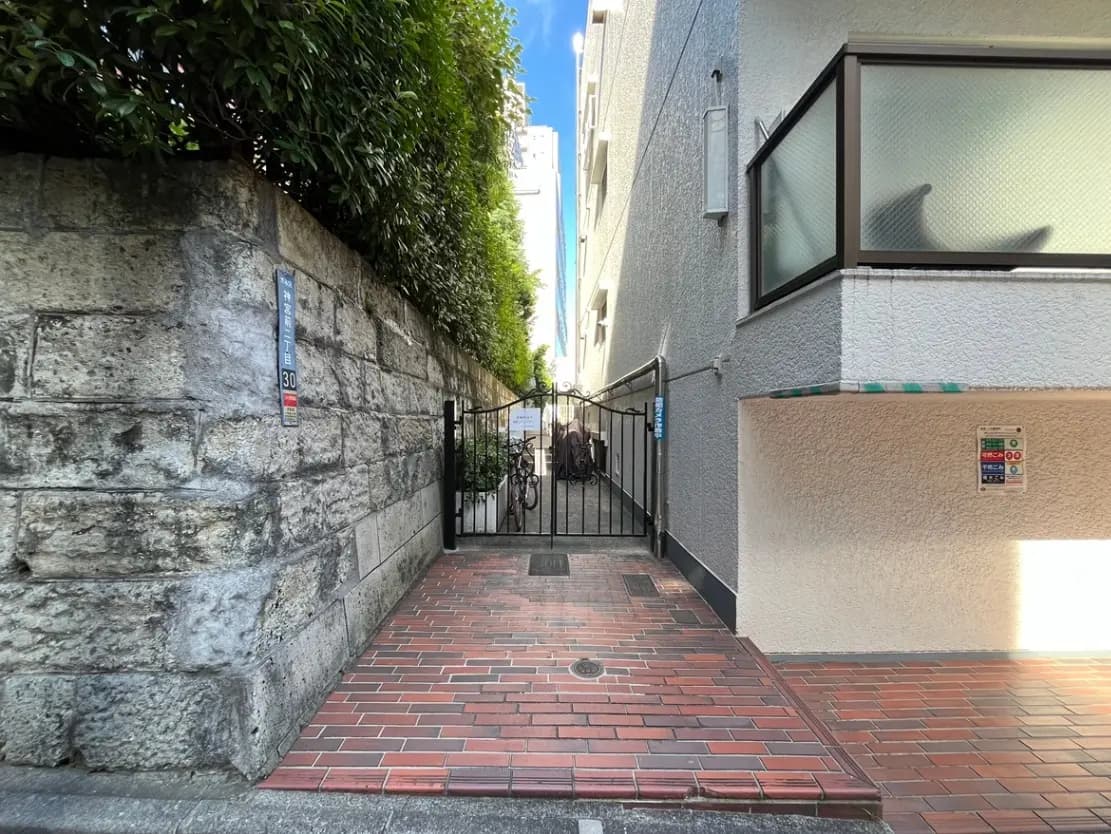 - 石積みの壁に囲まれた小道と自転車、開かれた gate と青空の背景、都会の住宅地の風景