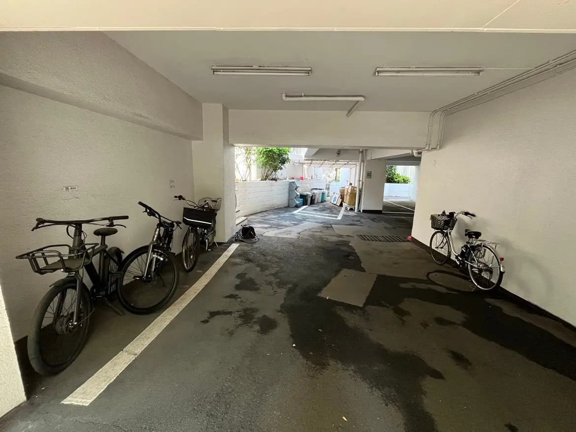 - 室内駐輪場に並ぶ自転車、白い壁とコンクリートの床、明るい照明のある空間