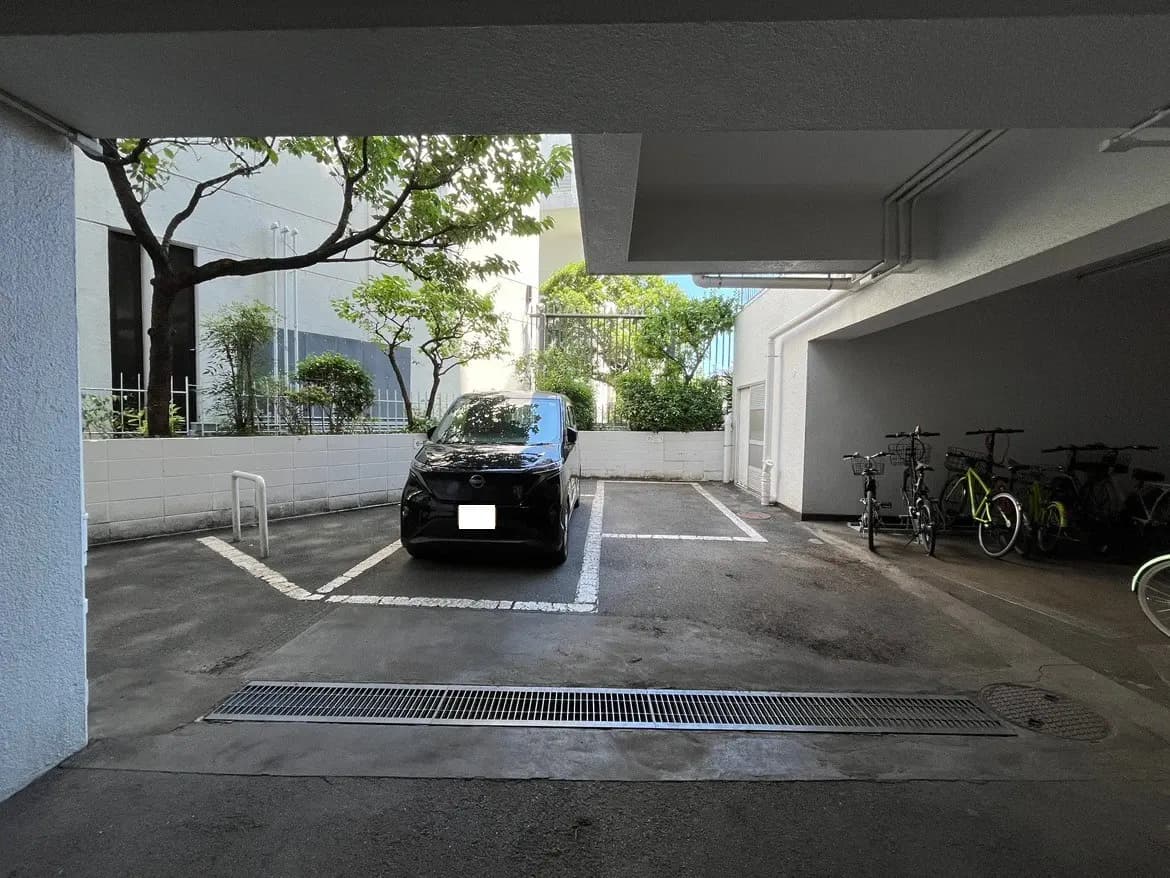 - スタイリッシュな黒の車が停まる駐車場、周囲に植栽が並び、奥に自転車が停まるスペースが見える景観