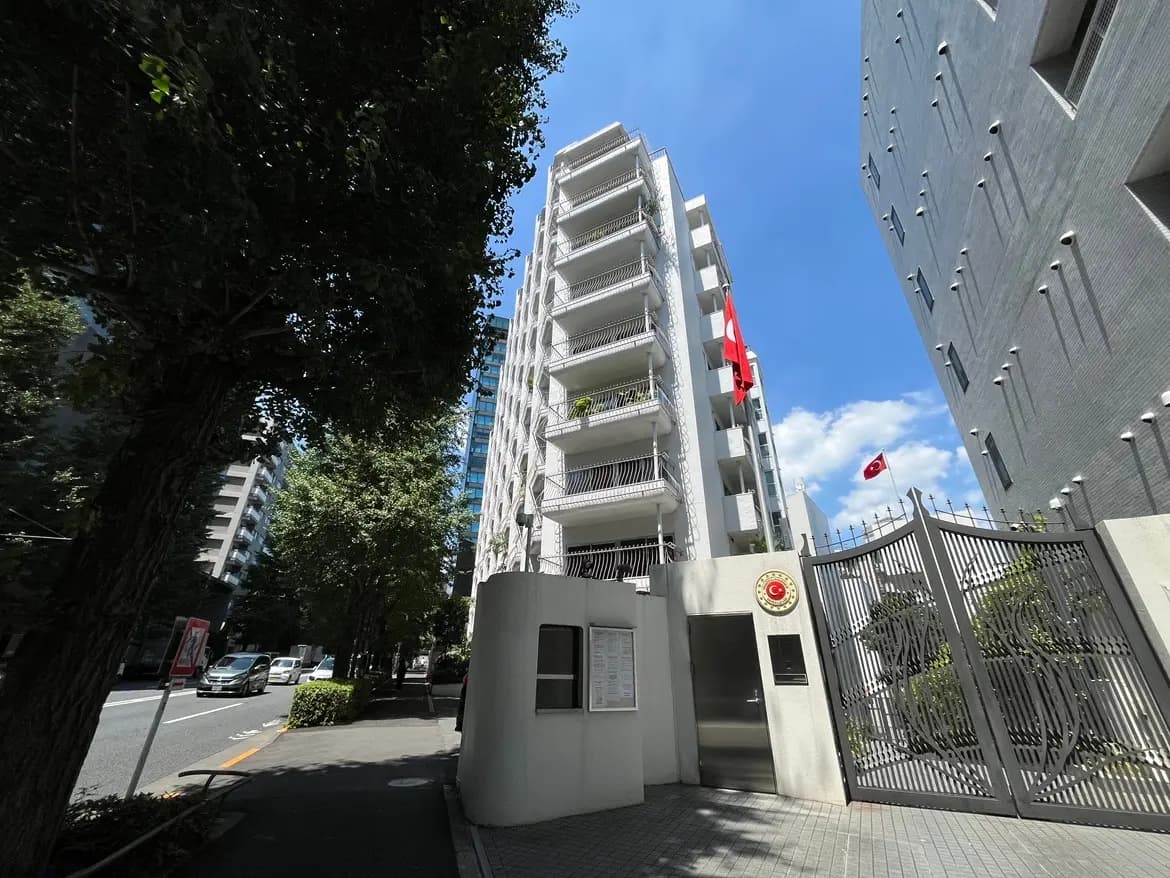 - トルコ大使館の建物、青空の下、植えられた木々と周囲のビルに囲まれたエントランスの外観