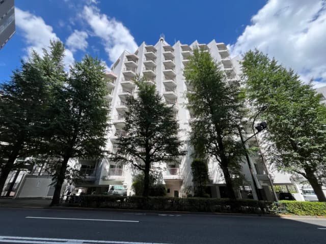 - 並木に囲まれた白い外壁のマンション、青空と白い雲が広がる風景