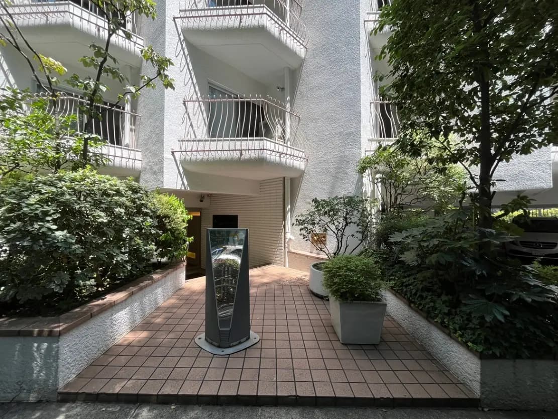 - 緑豊かなアプローチのあるマンション入り口、近代的なデザインのインフォメーションスタンドと植栽が配置された外観