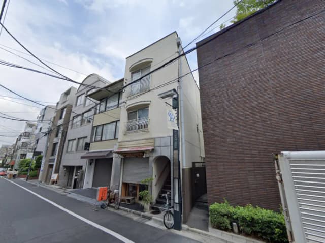 - 住宅街にある古いビルの外観、隣接するモダンな建物が並ぶ通りの景観、電線と標識が見える風景