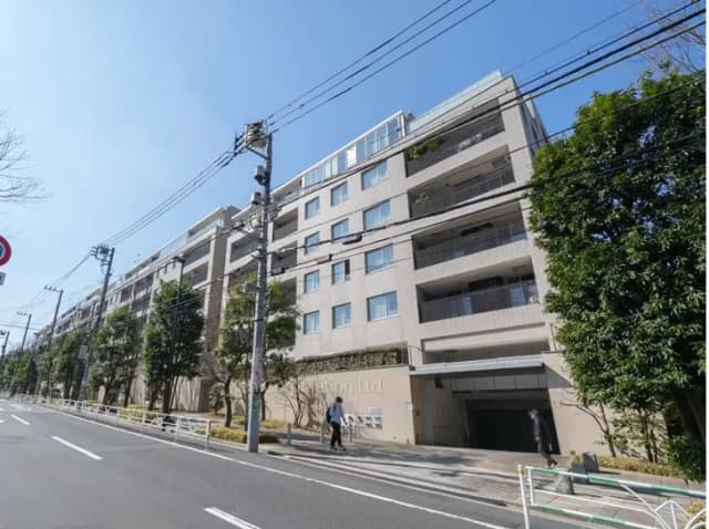 - 都市型マンションの外観、青空の下に広がるバルコニー付きのモダンな建物と周囲の緑豊かな木々