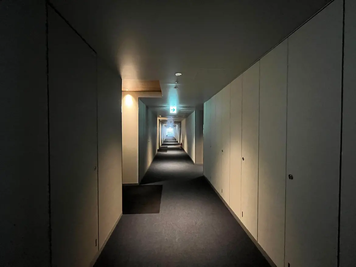 - 長い廊下、白い壁とドアが並び、照明が柔らかく反射する暗がりの風景