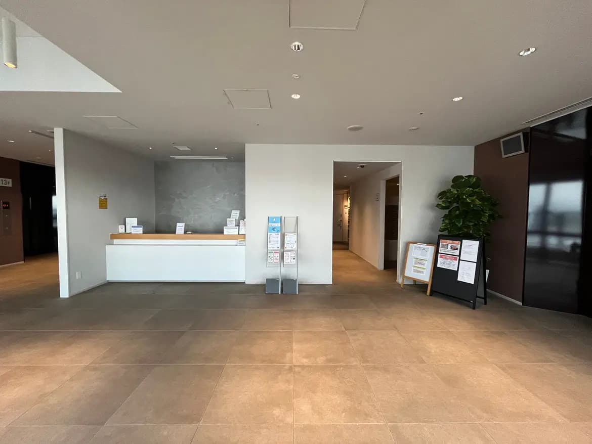 - モダンなデザインのフロントロビー、白いカウンターと案内板、広々としたスペースと明るい照明が特徴のインテリア