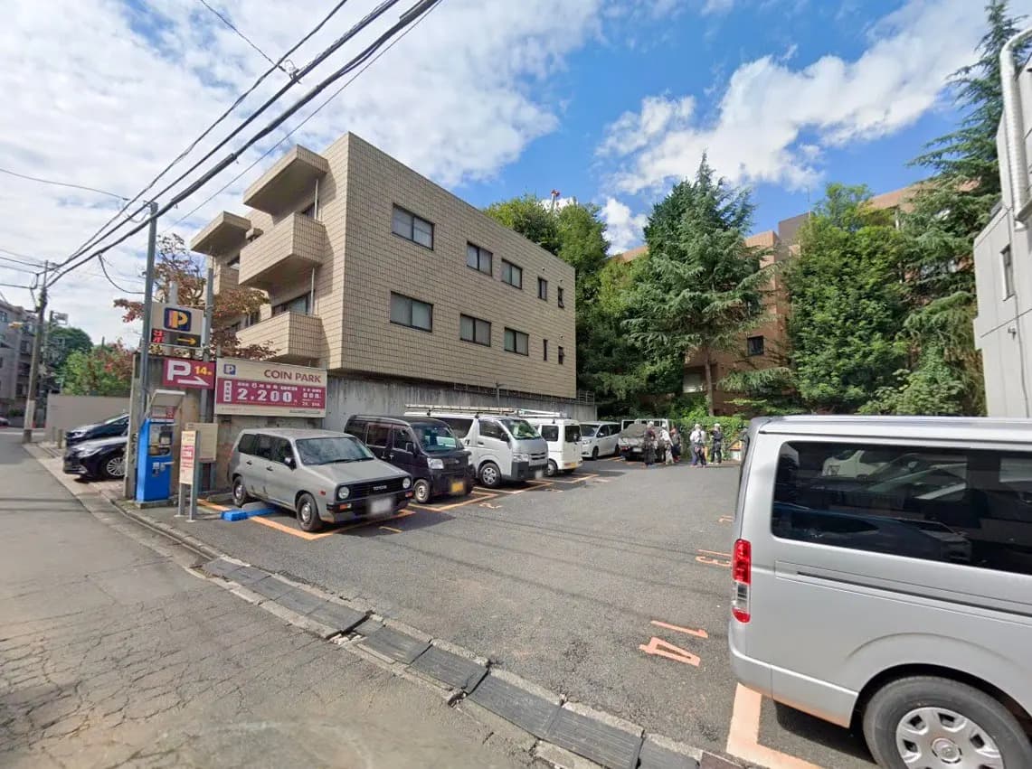 - さまざまな車両が停まっているコインパーキングの風景、背景にはマンションと木々が見える晴れた日