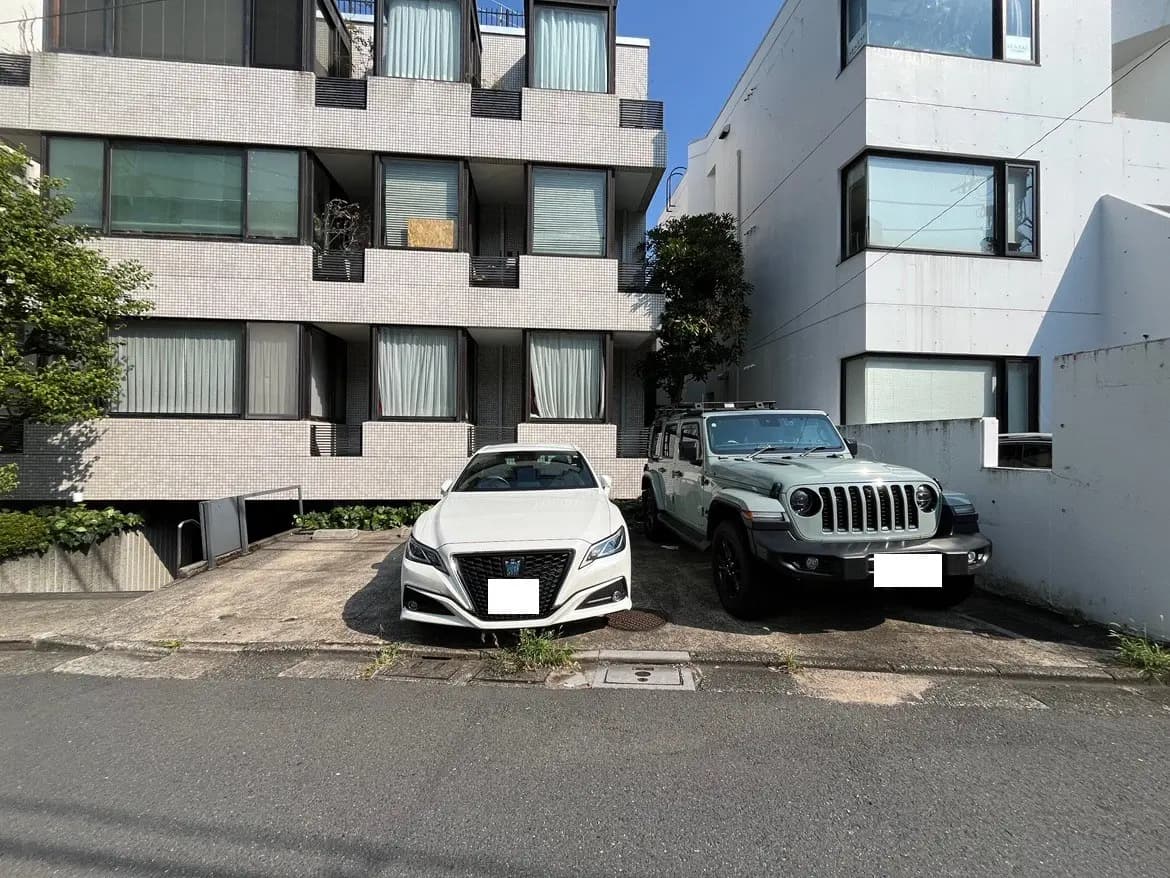 - 白い高級車とオフロード車が駐車された都市のアパートメント前の風景と明るい青空