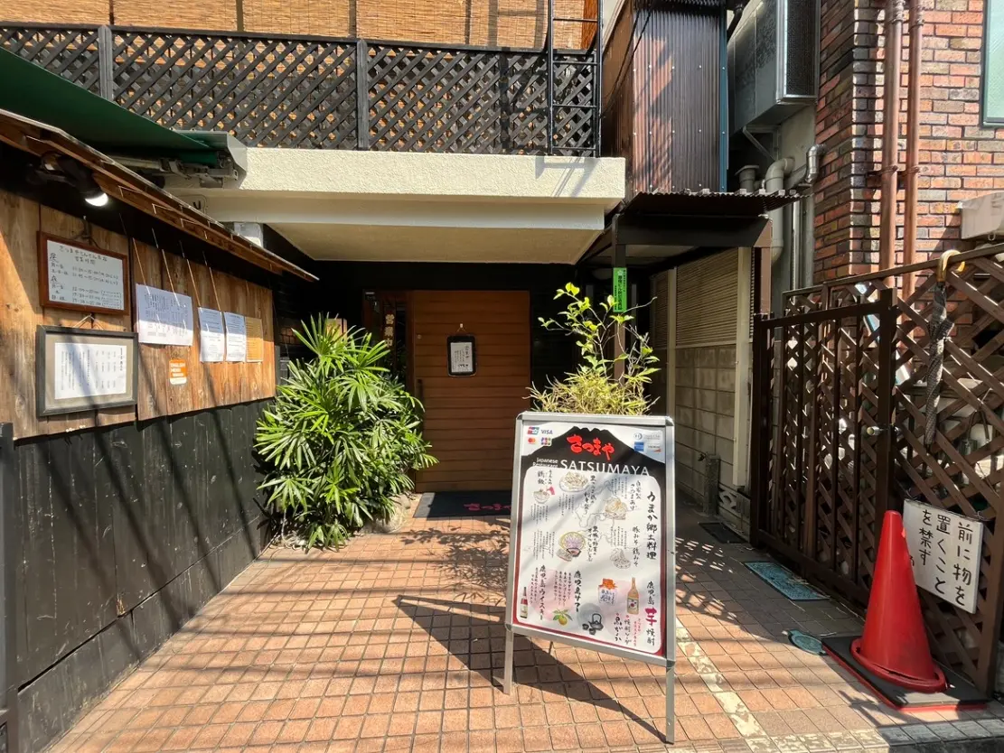 - レストランの入口、木製の看板とメニューが掲示され、植栽がアクセントになった外観の写真