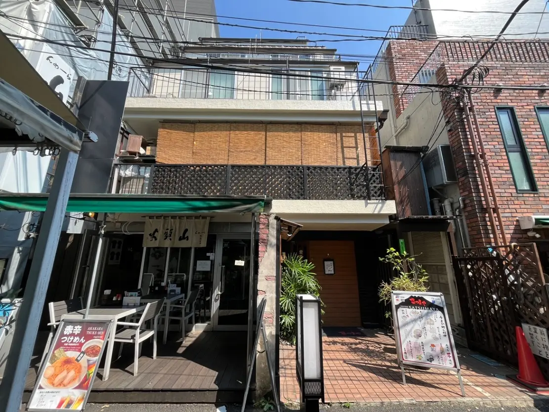 - 竹の飾りが施された和風の外観の飲食店、テラス席があり、周囲には観葉植物が配置されている風景