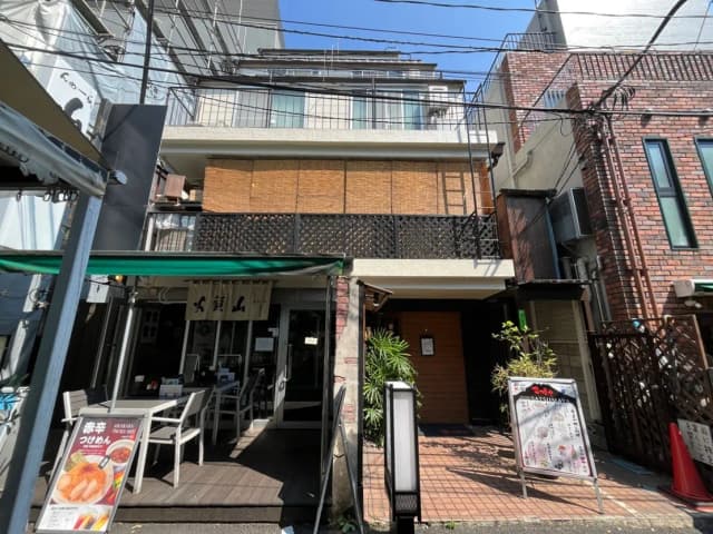 - 竹の飾りが施された和風の外観の飲食店、テラス席があり、周囲には観葉植物が配置されている風景