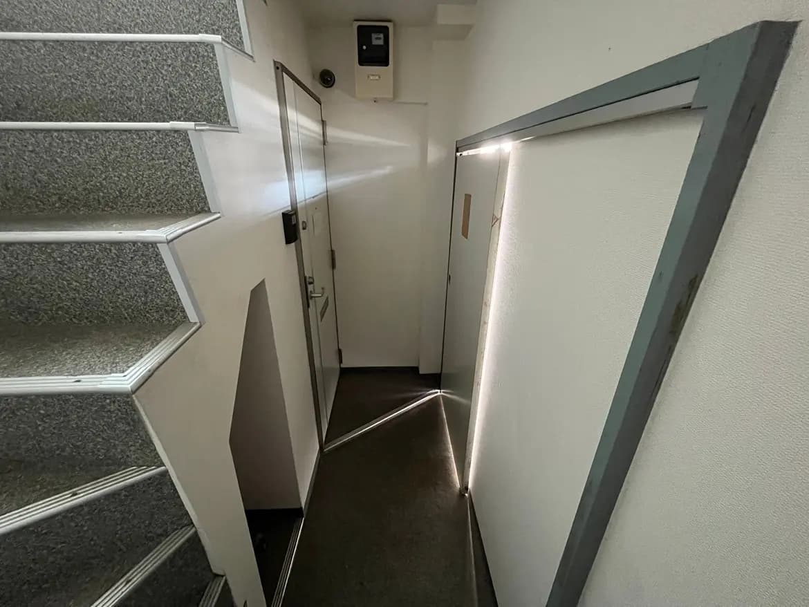 - シンプルなデザインの階段と廊下、明るい照明が差し込むドアサイズの空間、壁は白で整えられたインテリア