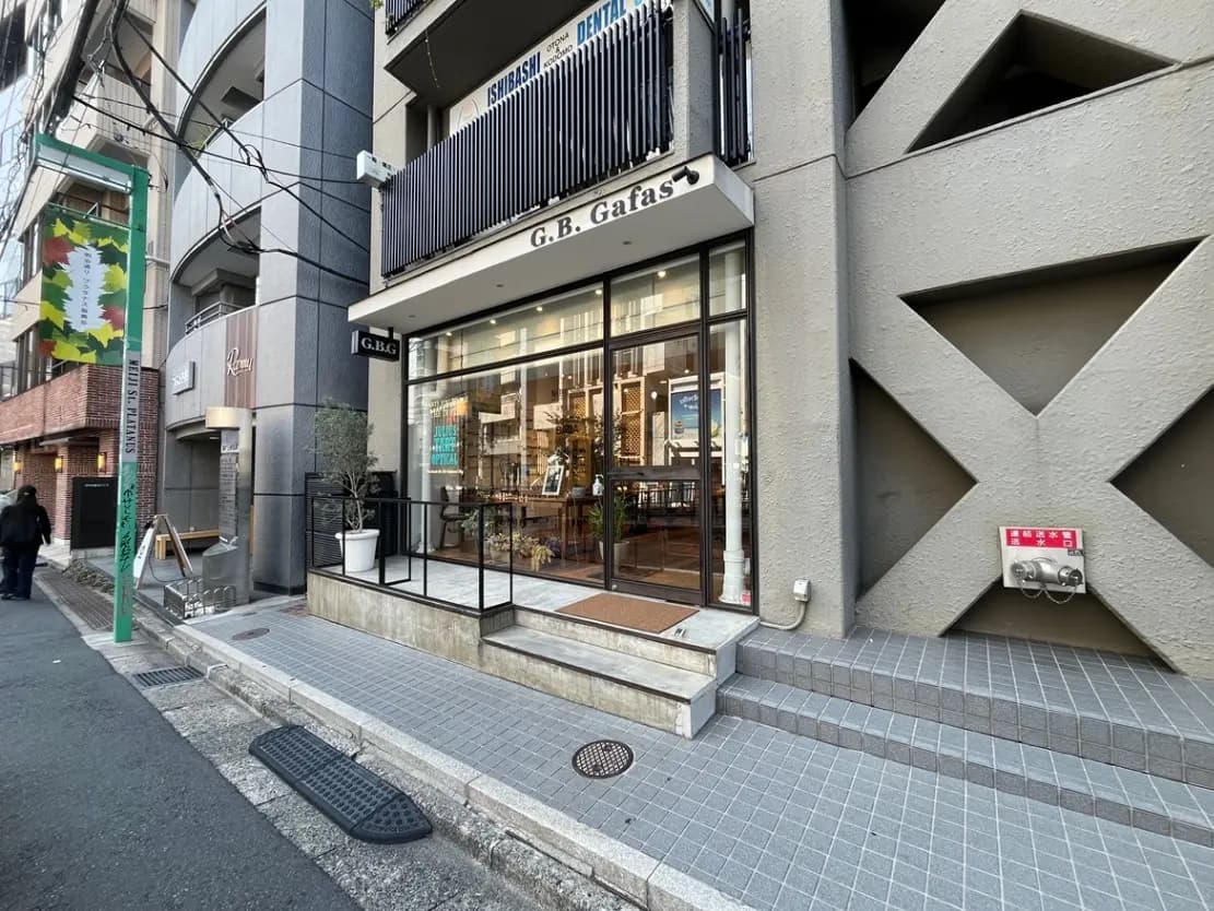 - モダンなデザインの店舗外観、広いガラス窓と階段のアプローチ、道沿いの歩行者と街灯の風景