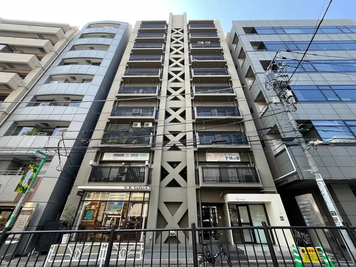 - 都市のモダンなビル群、黒いバルコニーを持つ8階建ての建物、下部にはカフェと歯科クリニックの看板が見える街並みの風景
