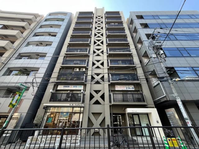 - 都市のモダンなビル群、黒いバルコニーを持つ8階建ての建物、下部にはカフェと歯科クリニックの看板が見える街並みの風景