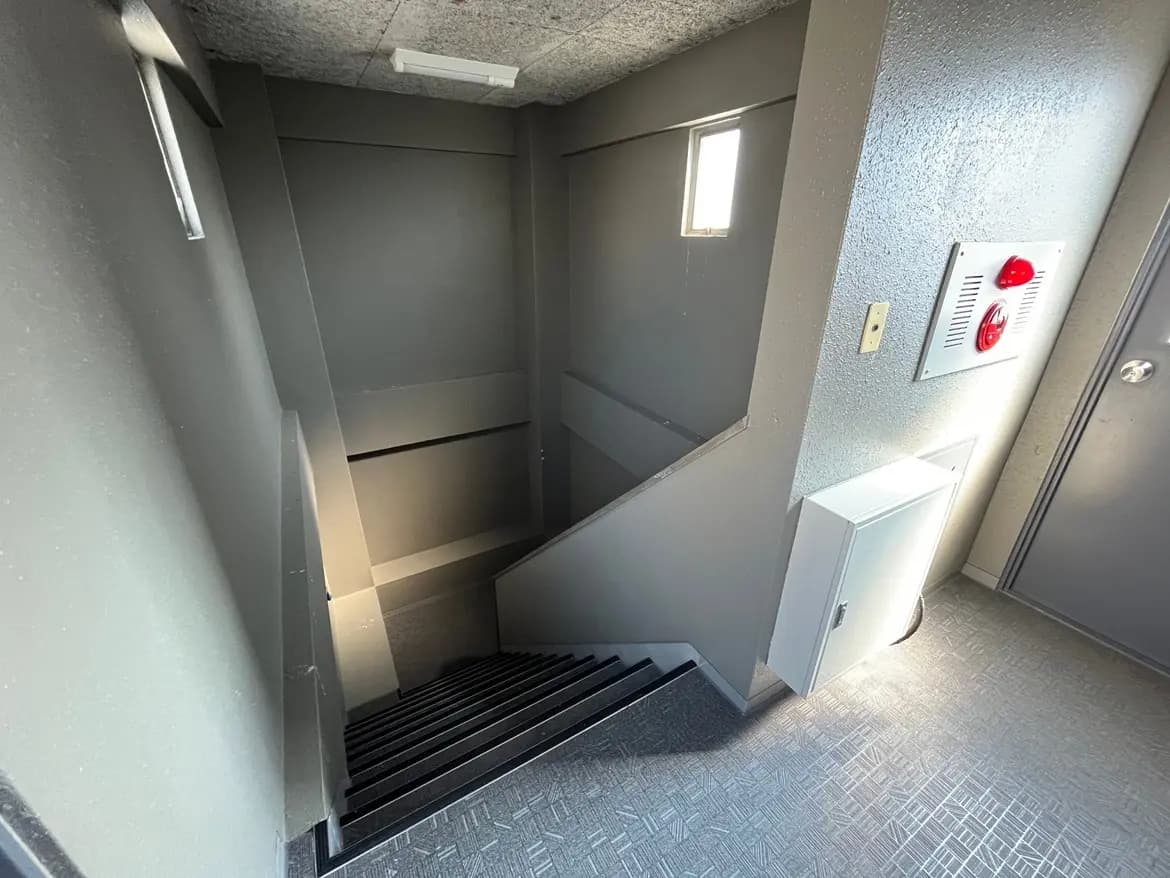 - 照明が差し込むモダンな階段の風景、暗い壁と無機質な内装が特徴的な設計