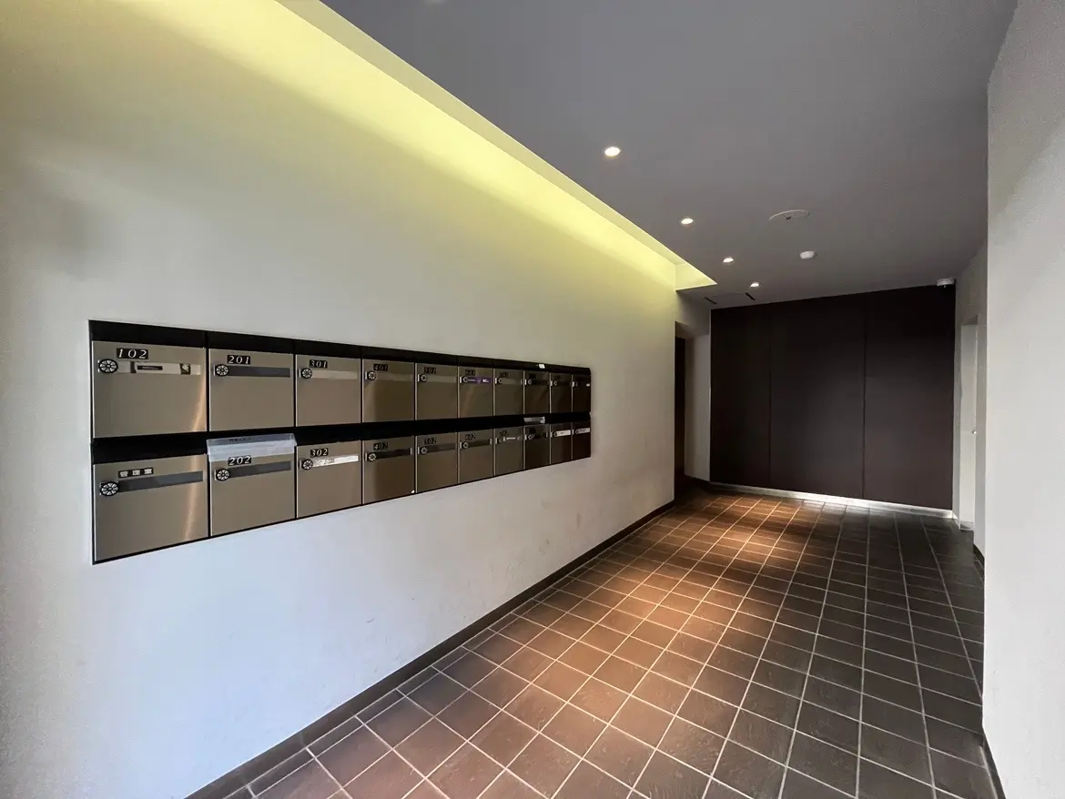 - モダンなデザインの集合住宅のエントランス、金属製の郵便受けが設置された壁とタイルの床、照明が施された通路