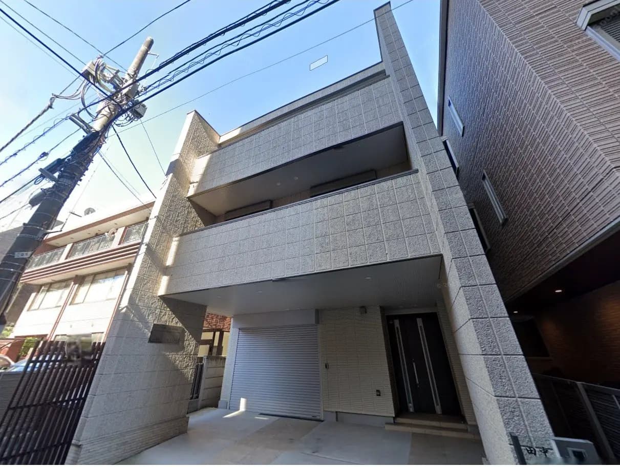 現代的なデザインの3階建て住宅、白い外壁と大きなバルコニー、周囲に電柱が立つ街並みの景観