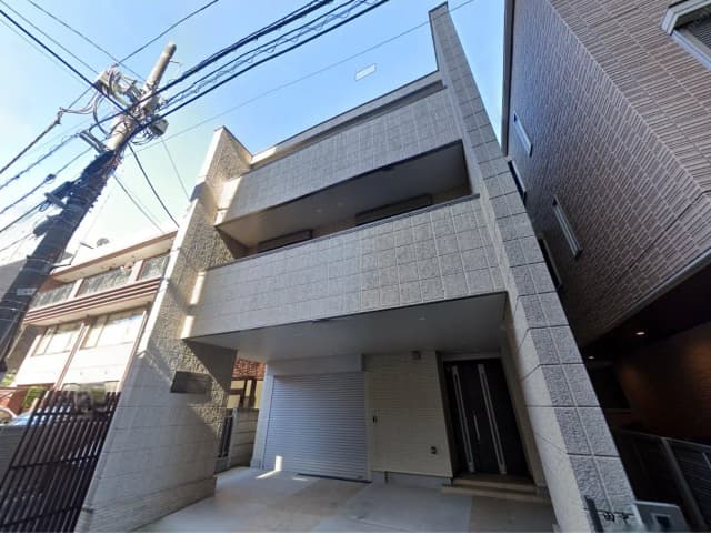 現代的なデザインの3階建て住宅、白い外壁と大きなバルコニー、周囲に電柱が立つ街並みの景観