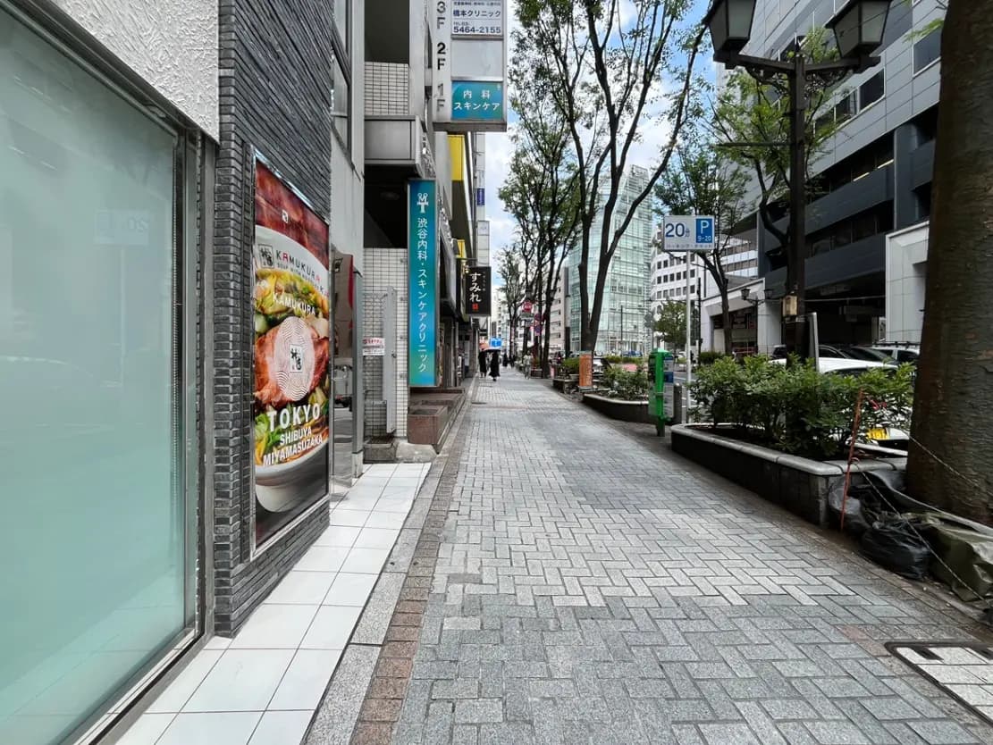 - 渋谷の街並み、舗装された歩道と店の看板、緑の木々が並ぶ通りの風景