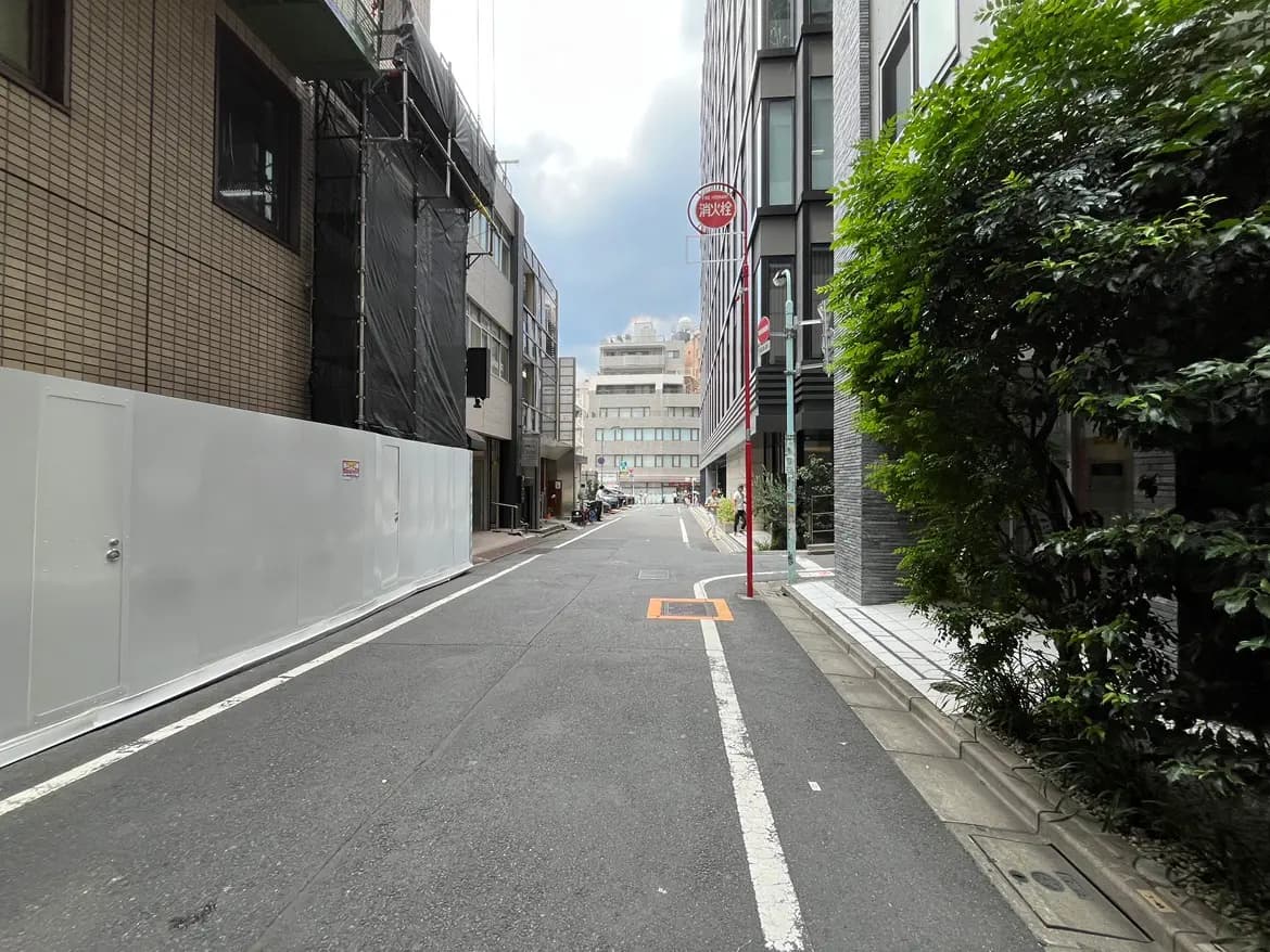 - 都市の風景に見える工事中の建物と緑の木々が並ぶ歩道、広い道路と曇り空の背景