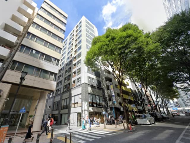 - 都会的な風景、商業ビルと緑豊かな街路樹が並ぶ通り、賑わう歩行者と車両の様子