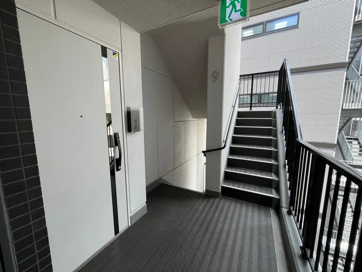 - モダンなマンションの廊下、エレベーターのドアと階段が見えるシンプルで明るいエントランスの風景
