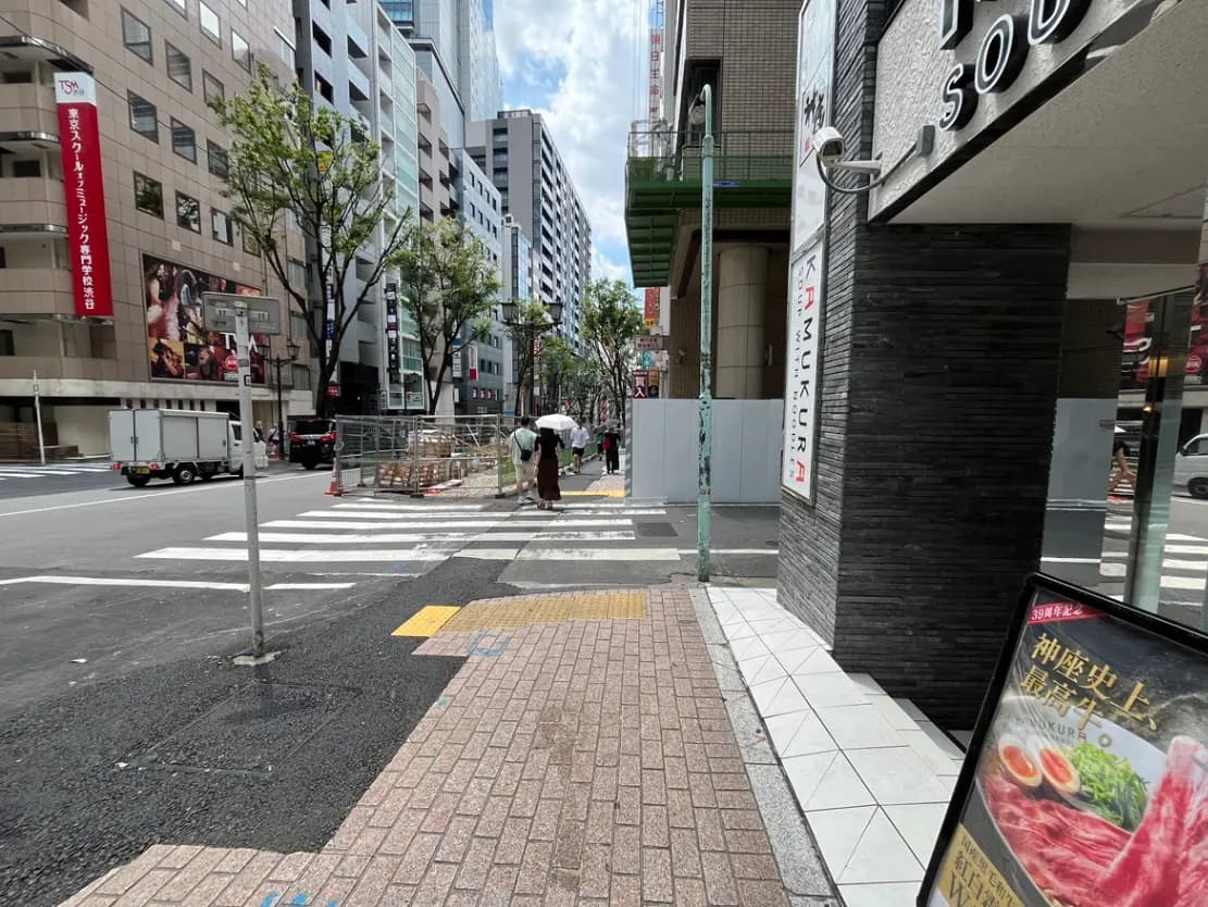 - 都会の交差点、歩道に傘を持った人々と道路工事の様子、ビルに囲まれた風景