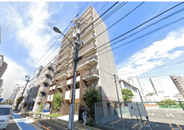 - 都市部に位置するモダンなマンション、外観はシンプルなデザインで、周囲には電柱や緑地がある風景