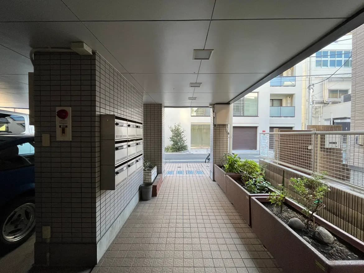 - モダンなマンションのエントランス、郵便ポストが並び、植栽が施された明るい通路のインテリア