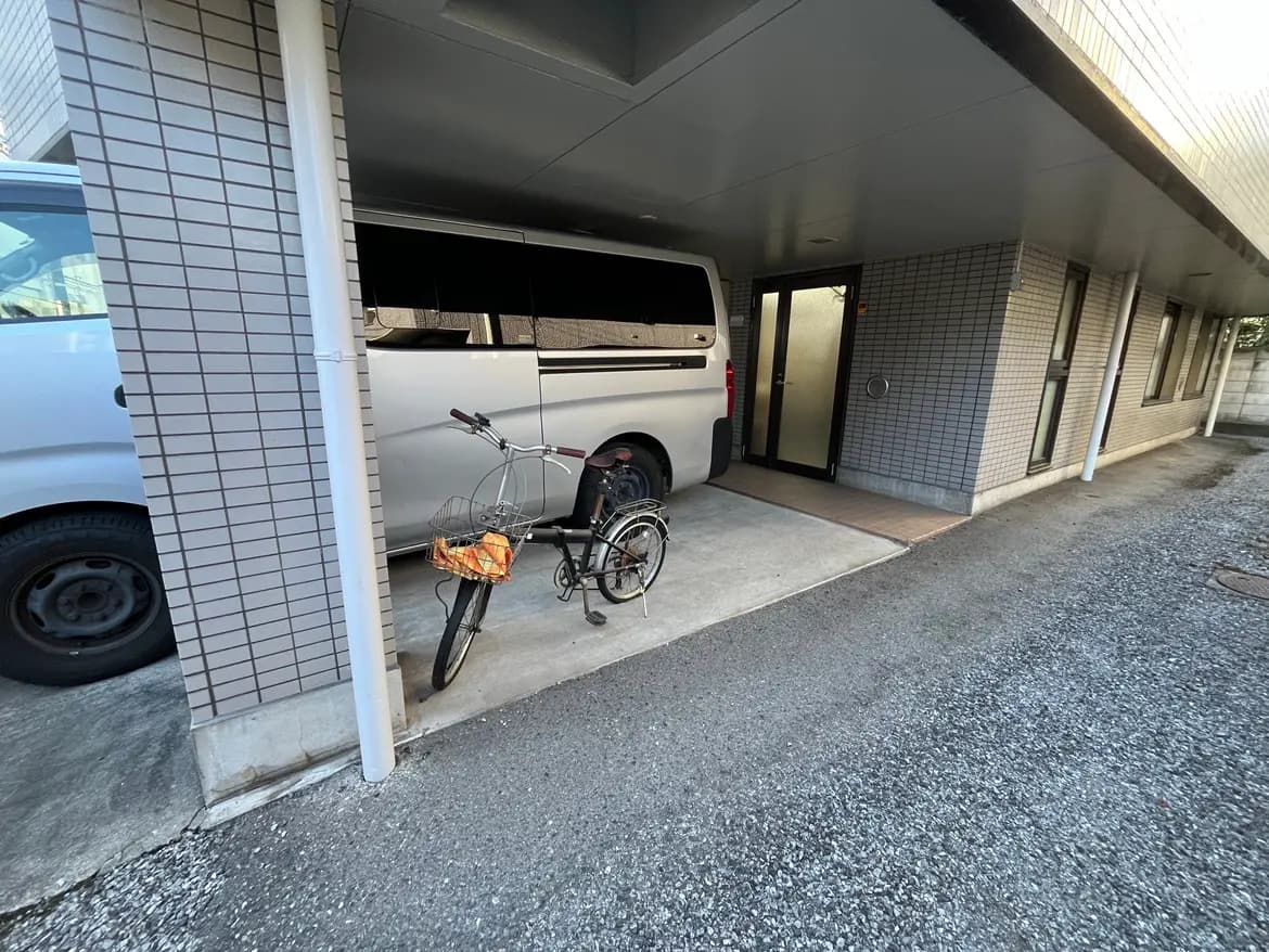 - 駐車スペースに停められた白いバンと自転車、建物のエントランスが見える景観