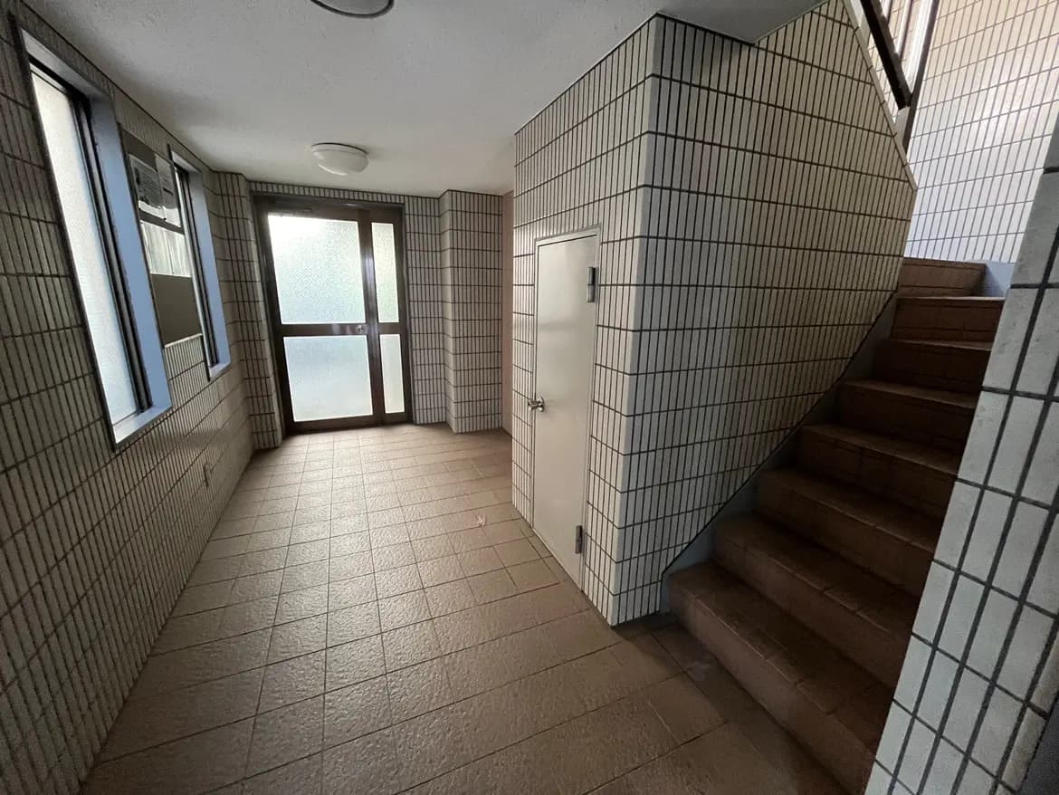 - 照明のある明るい入口、タイル張りの床、階段とドアのあるシンプルな建物の内部空間