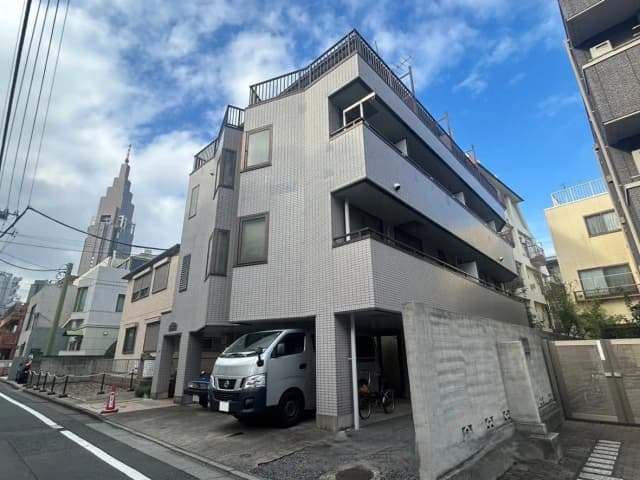 - 都市型のモダンなアパートメントビル、隣接する建物と東京の高層ビルが見える景観、空は曇り気味の青色