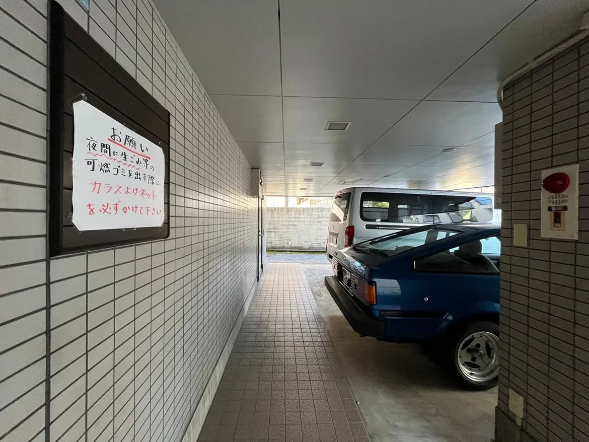 - 駐車場の通路と2台の車、壁に貼られたごみ出しの注意書きがある風景