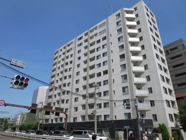 - 青空の下、住宅街に立つモダンなマンションの外観、白い壁とバルコニーが特徴的な7階建ての建物